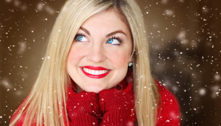 blond girl with a big toothy smile, red lipstick, gloves and sweater with light snow falling