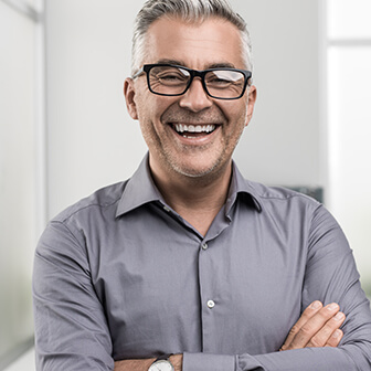 a man with glasses in a gray button down shirt smiling with partial dentures