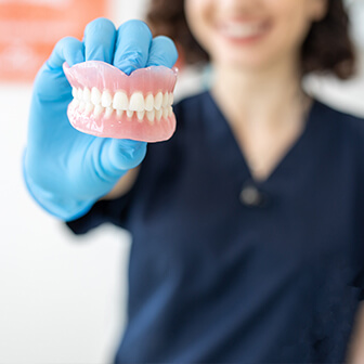 a dental hygienist holding up a set of upper and lower dentures
